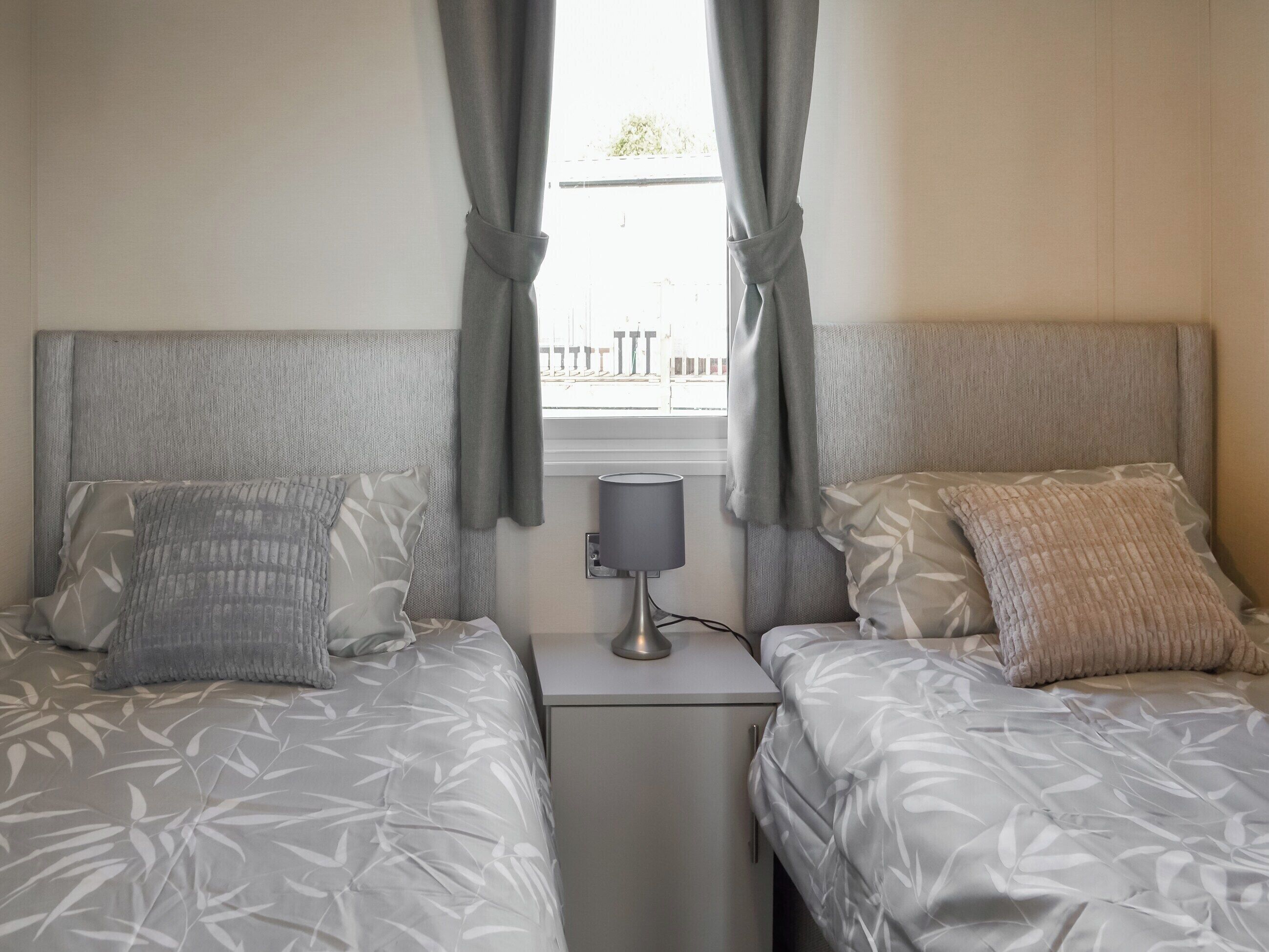 A twin room with two beds, each with a patterned bedspread, a bedside table with a lamp, and a window with curtains.