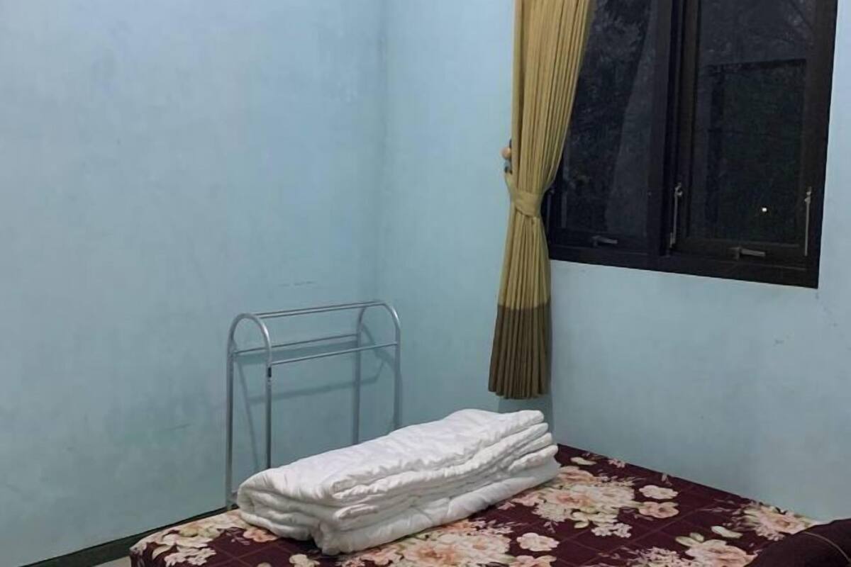 A small room with a metal bed frame, a floral-patterned bedspread, and a window with a curtain.