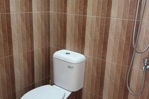 A bathroom with a toilet, a shower, and a wall with vertical stripes. - Green Homestay (Junrejo)