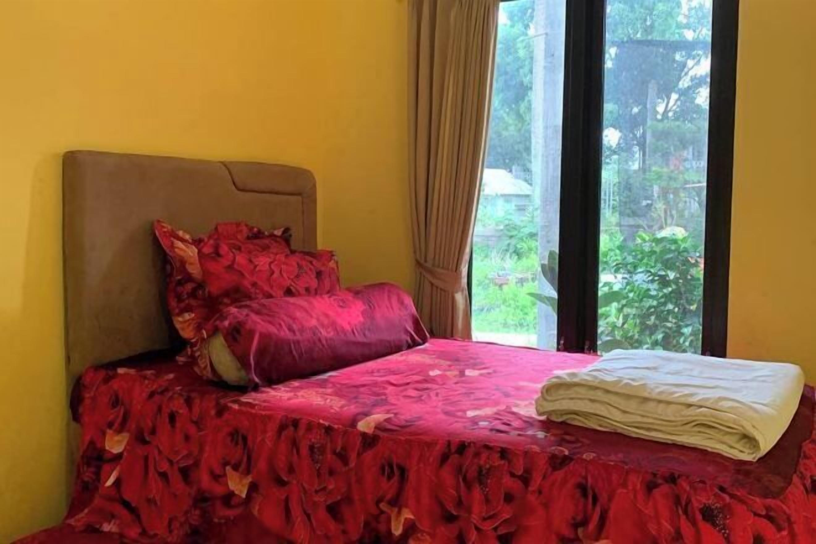 A room with a bed, a window with curtains, and a view of greenery outside.