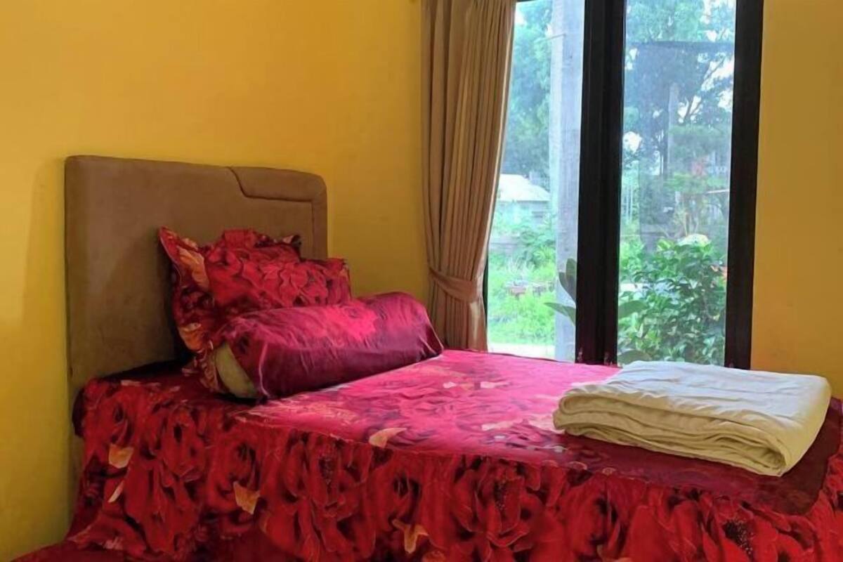 A room with a bed, a window with curtains, and a view of greenery outside.