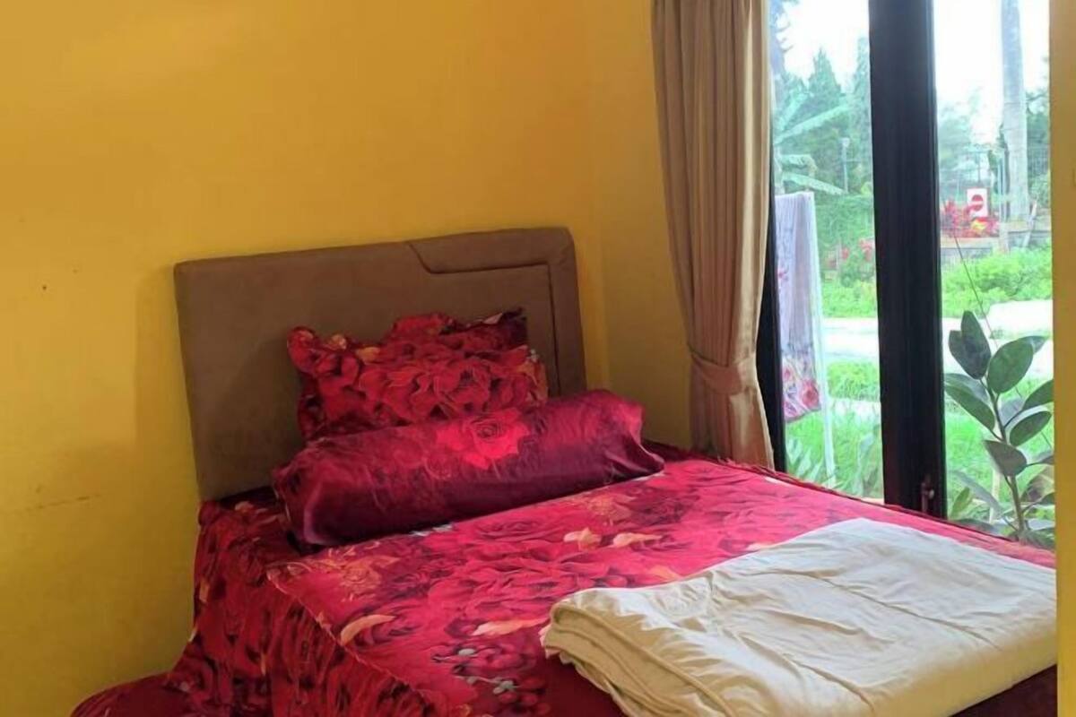 A bed with a floral bedspread and a white blanket, a brown headboard, and a view of greenery outside.