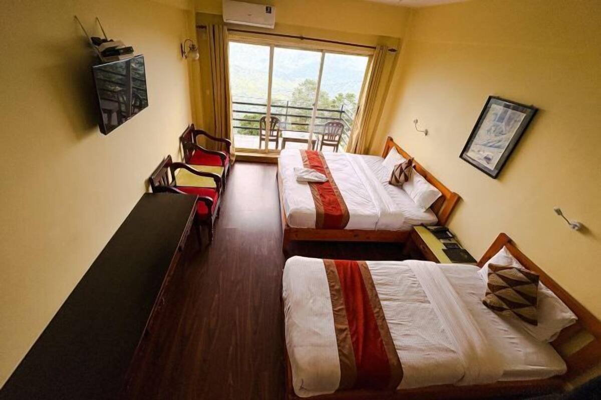 A hotel room with two beds, a desk, a chair, a TV, and a balcony with a view.