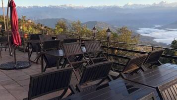 Un área de estar al aire libre con mesas y sillas, con vistas a un paisaje montañoso.