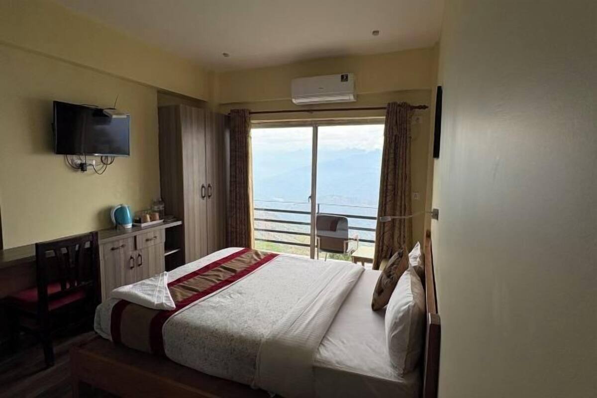 A hotel room with a bed, a TV, a desk, and a view of the sea.