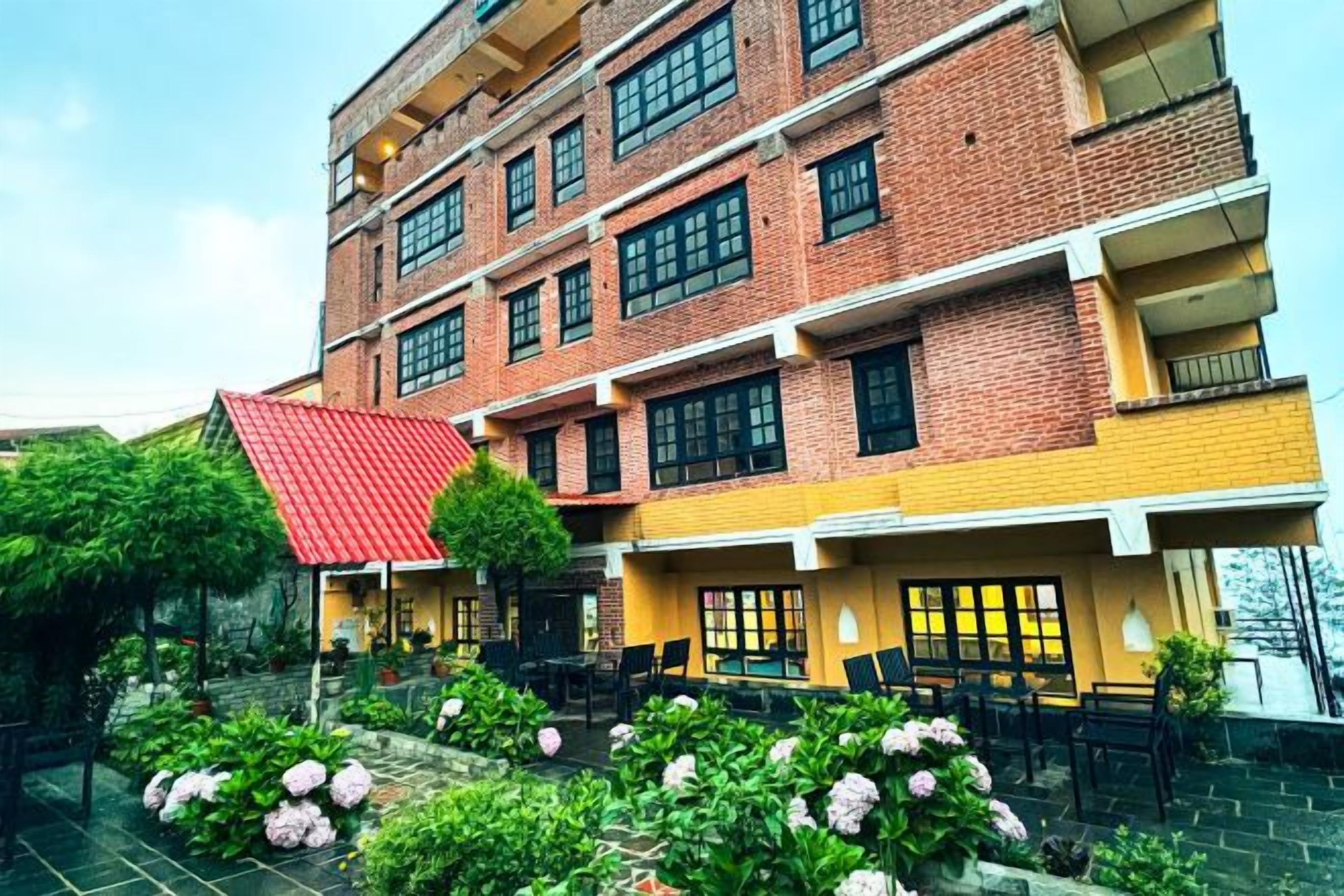 Un edificio de varios pisos con techo rojo, fachada de ladrillo y un patio con mesas al aire libre.