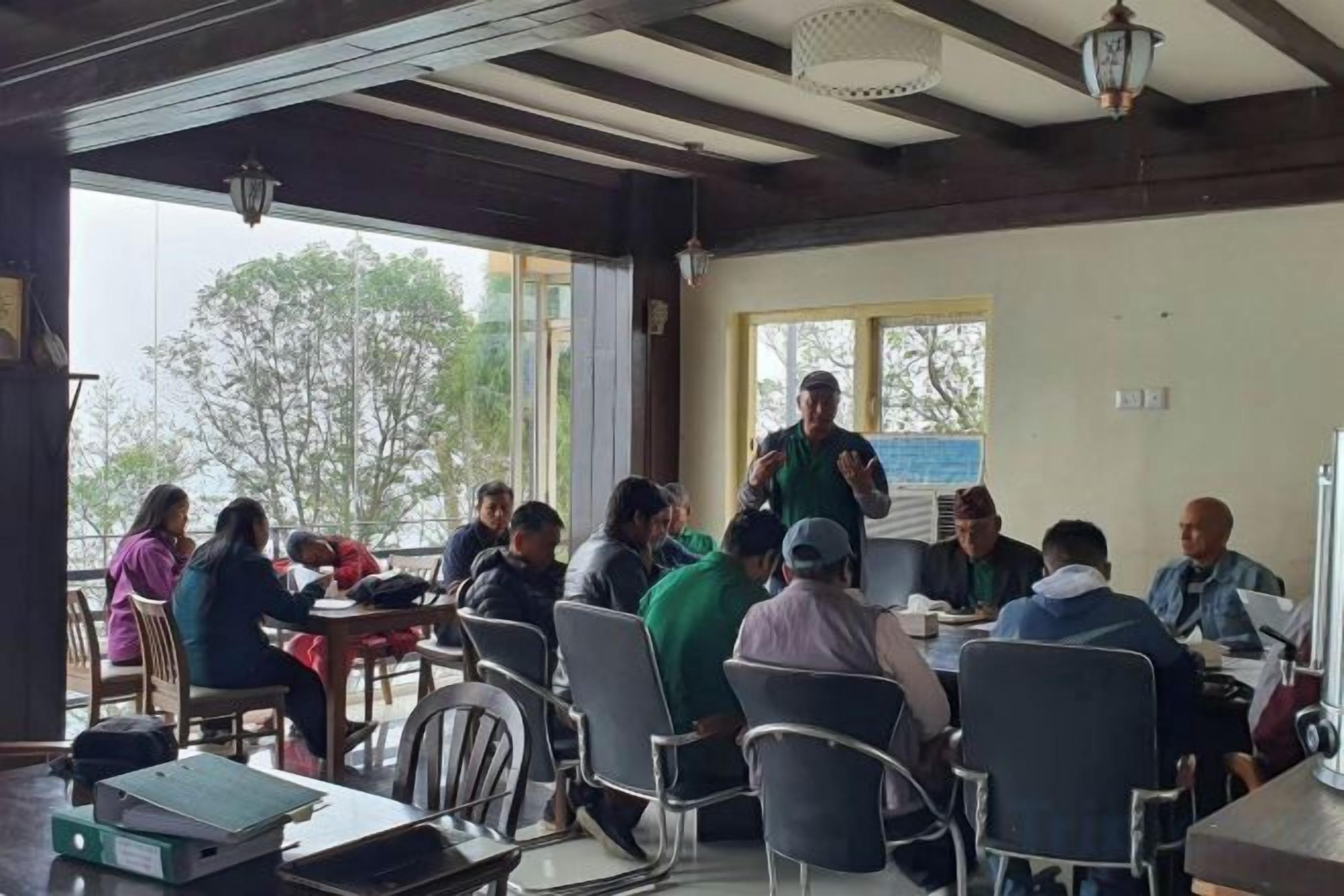 Un grupo de personas sentadas alrededor de una mesa en una habitación con vistas a árboles.