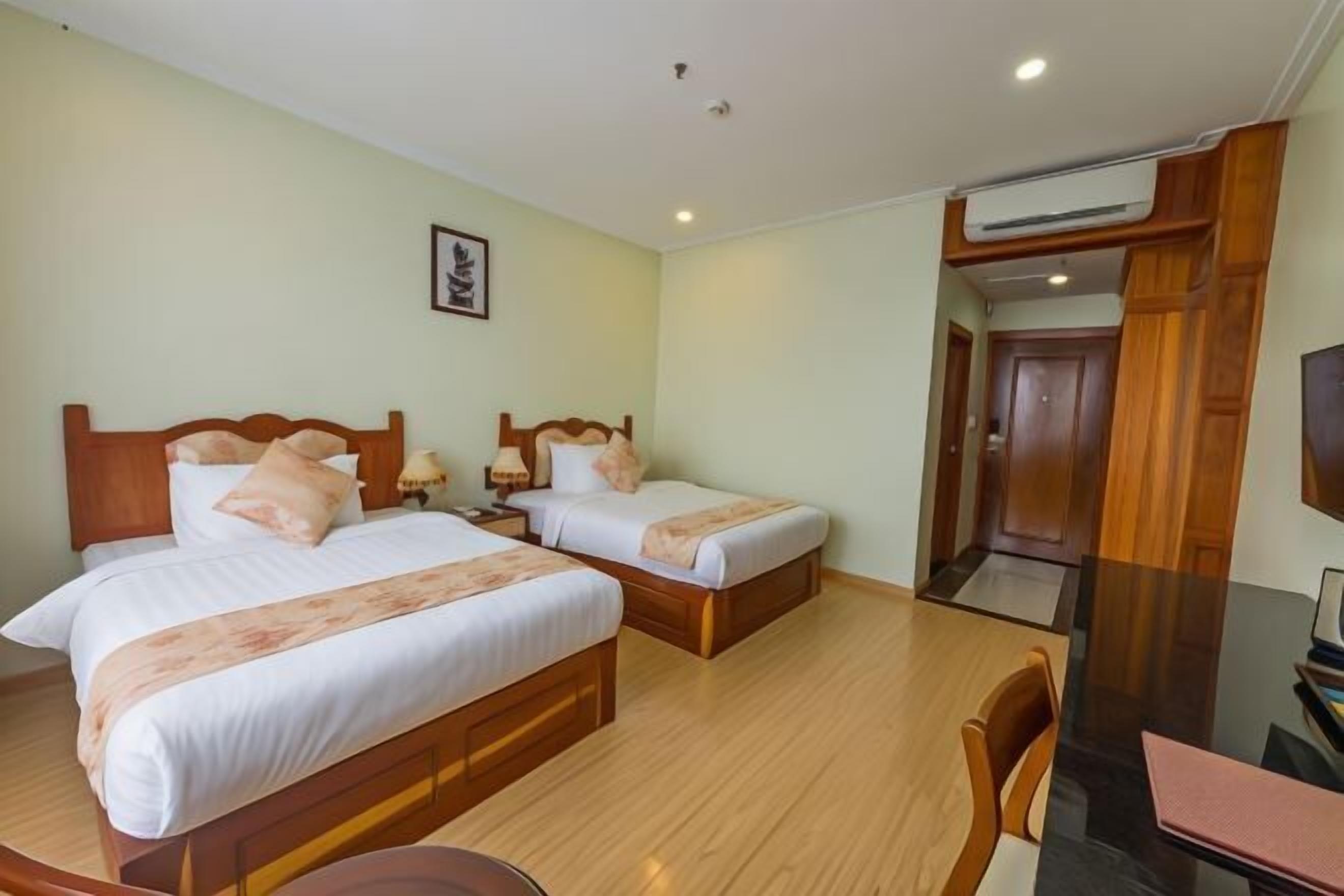 Une chambre d’hôtel avec deux lits en bois, un bureau avec une chaise et un téléviseur.