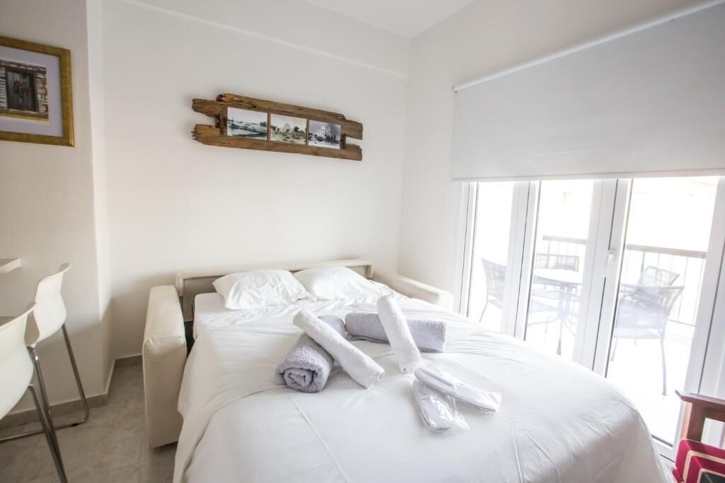 A hotel room with a bed, a chair, and a balcony with outdoor furniture.