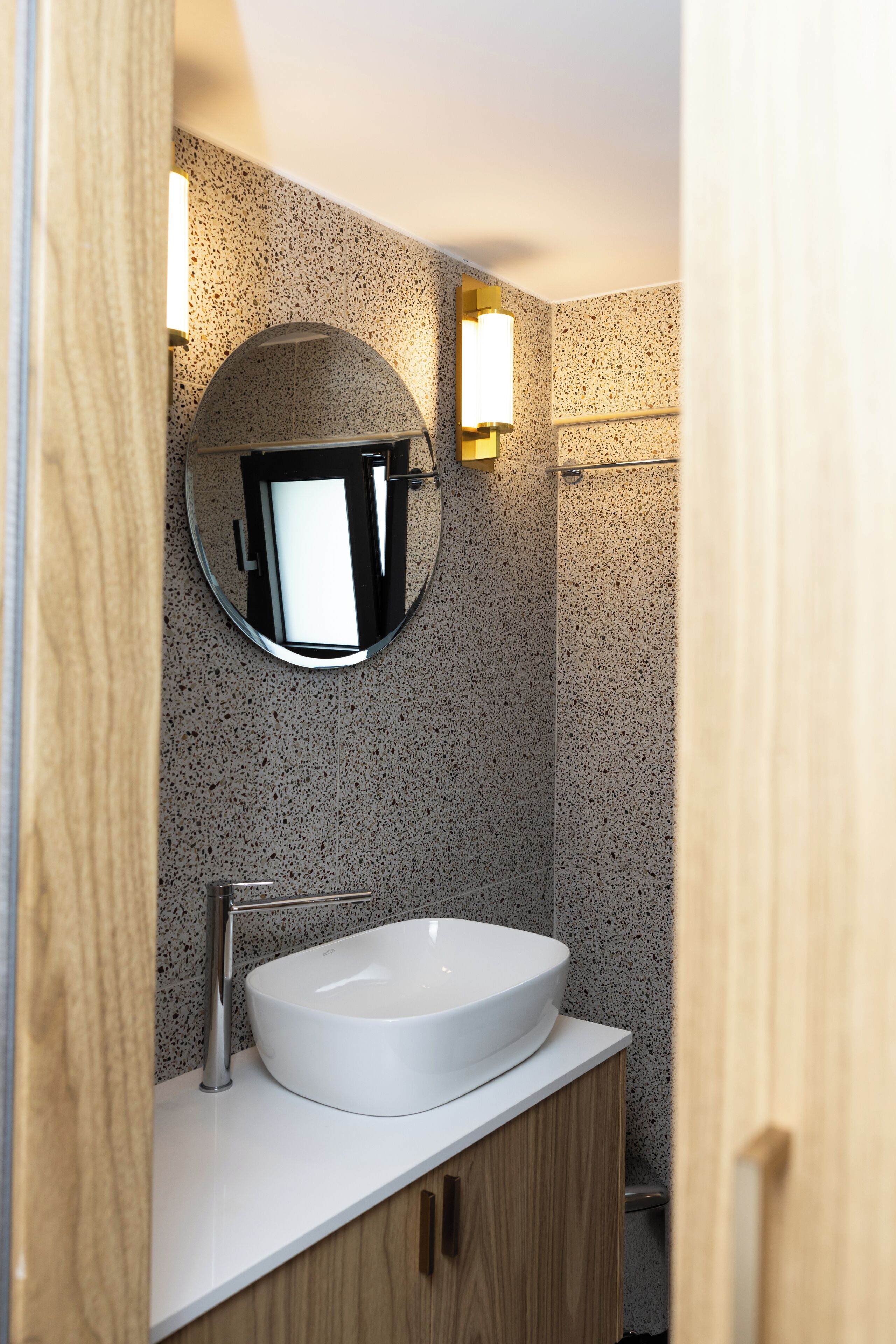 A bathroom with a round mirror, a white sink, and wooden cabinets.