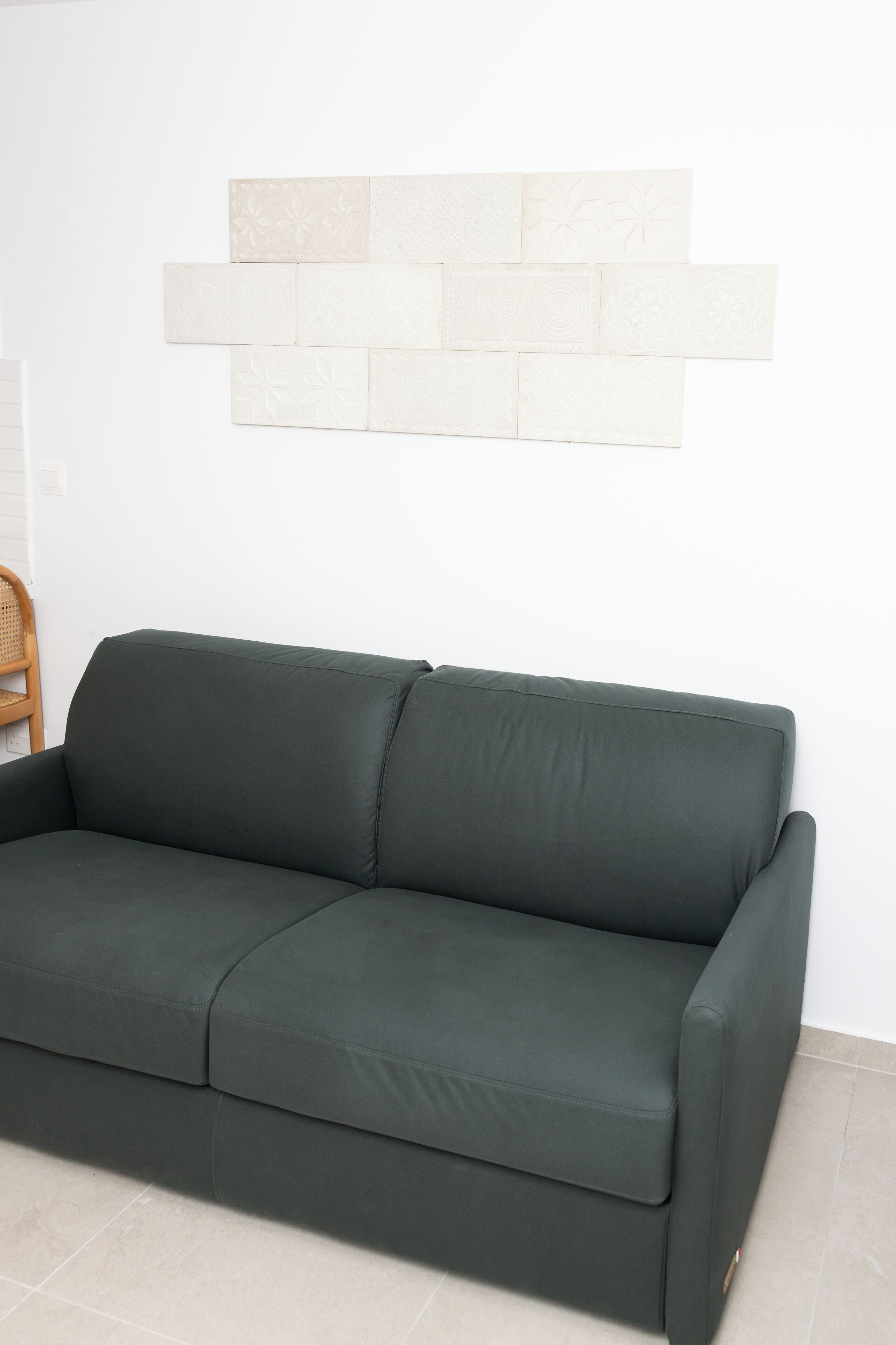 Un canapé vert foncé est placé contre un mur blanc, et un pare-feu en carreaux de couleur claire se trouve derrière.