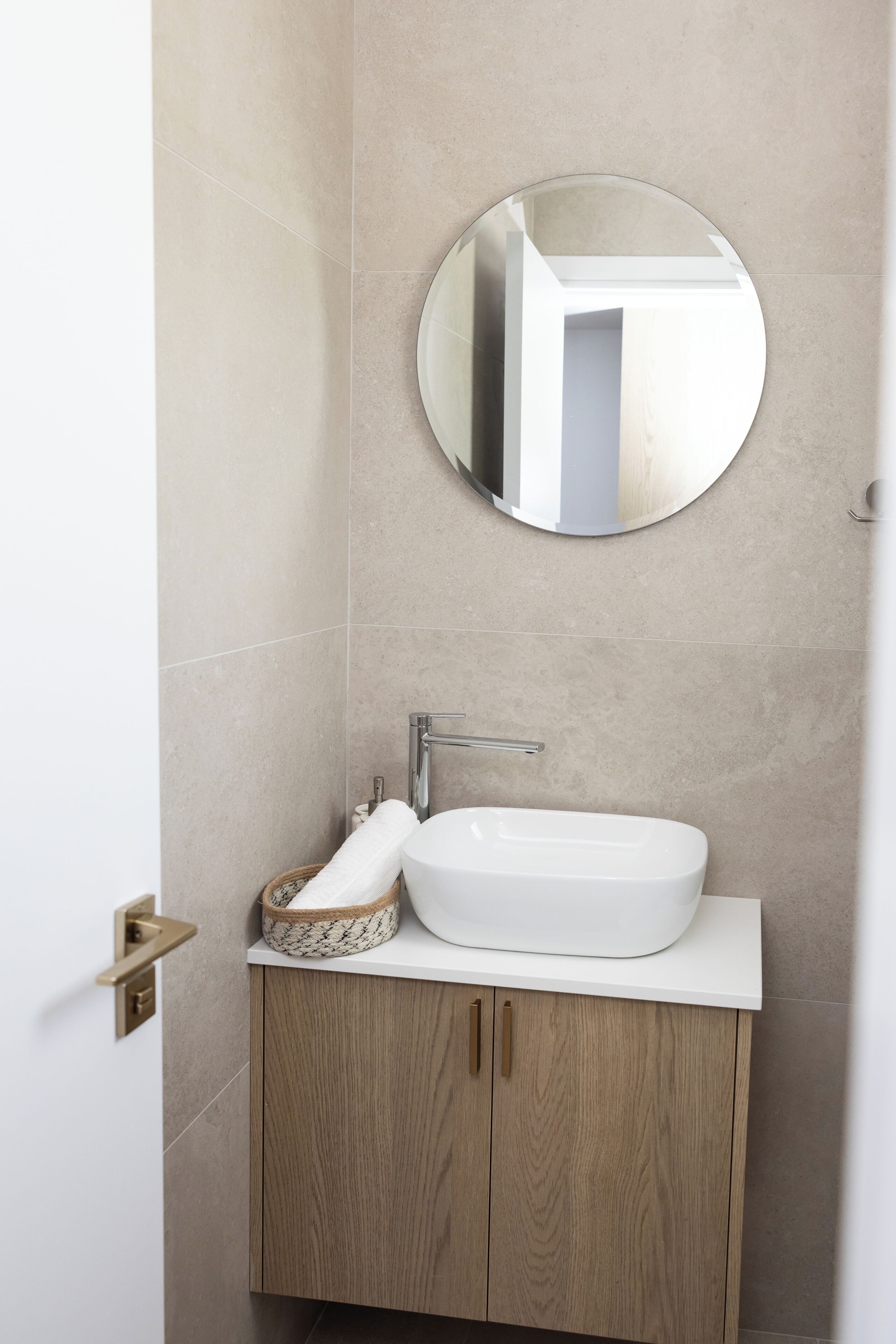 Une salle de bain avec un miroir rond, un lavabo blanc et des meubles en bois.