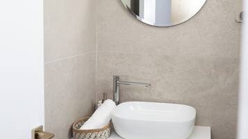 Une salle de bain avec un miroir rond, un lavabo blanc et des meubles en bois.