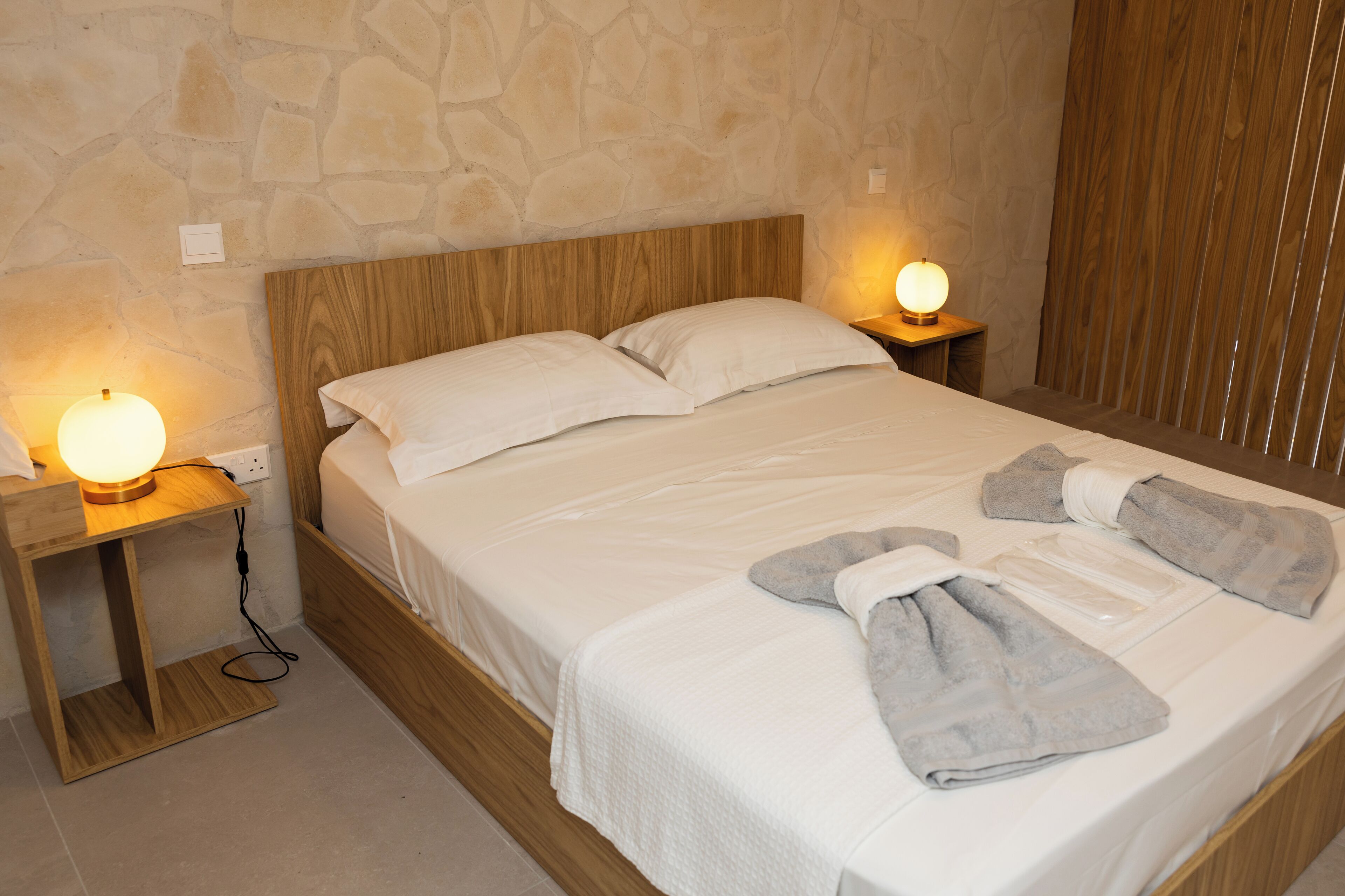 A neatly made bed with white linens, two bedside lamps, and a set of towels on the bed.
