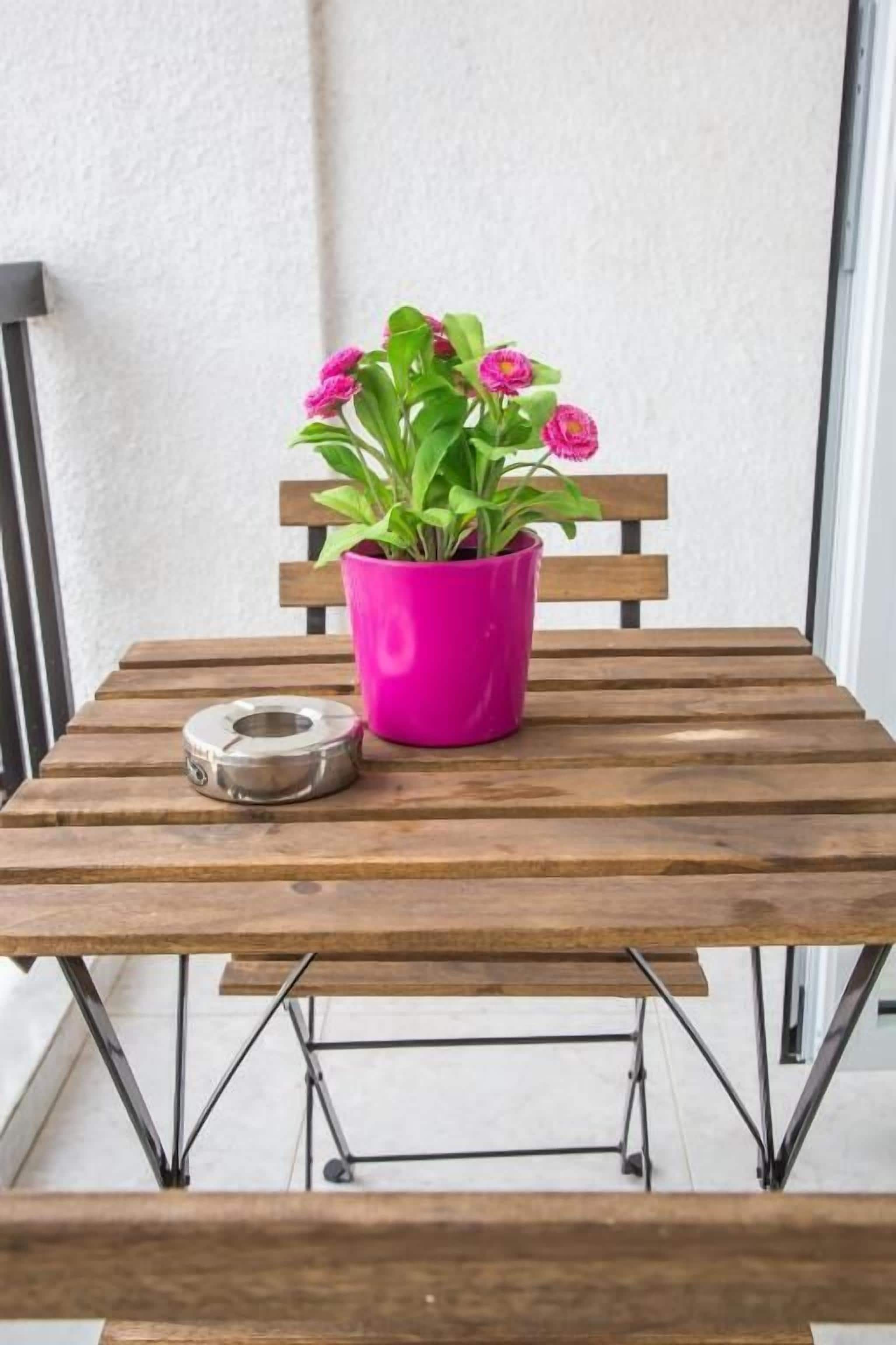 A wooden table with a pink pot of flowers and a metal object on it.