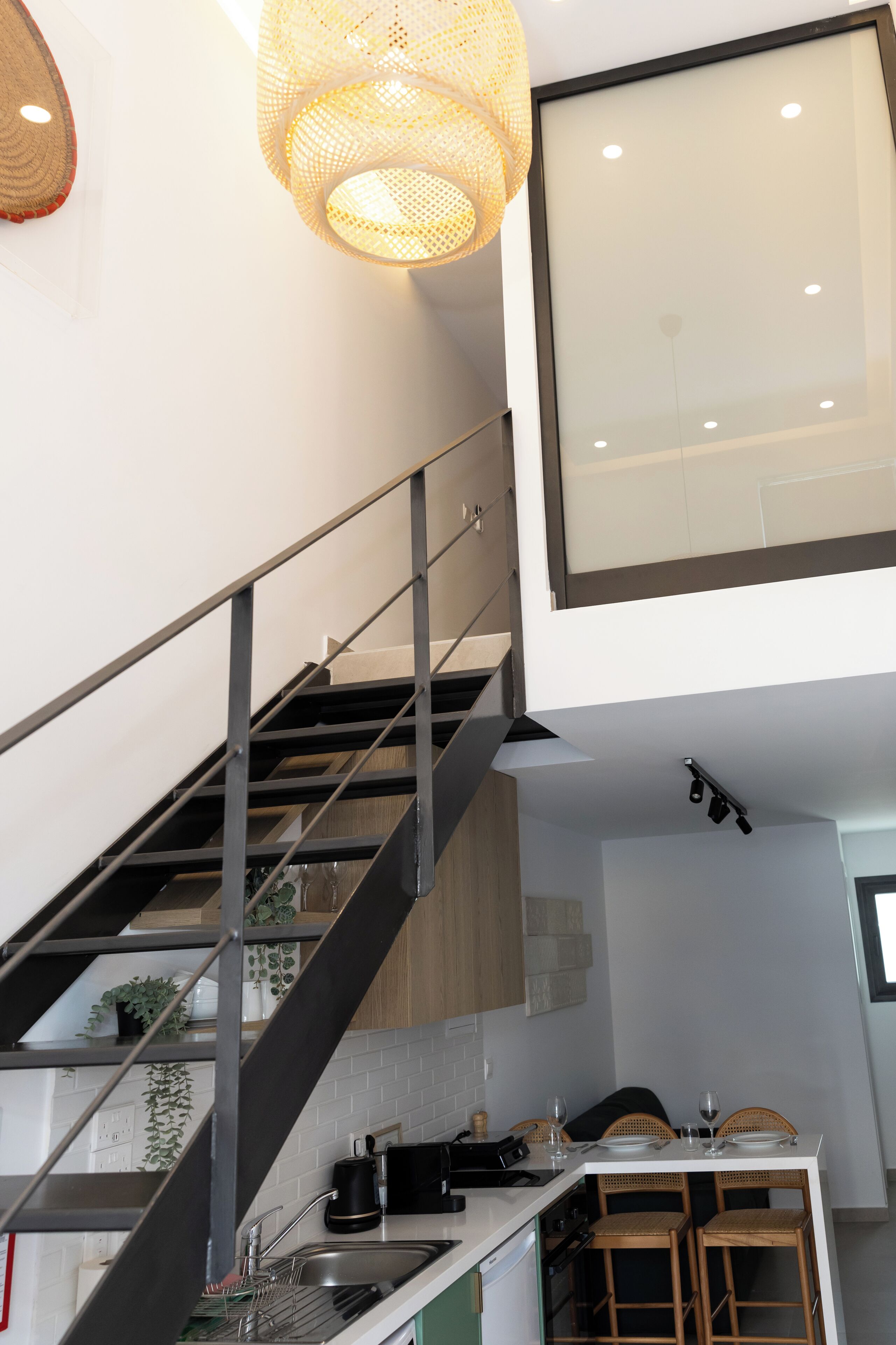 A modern kitchen with a staircase, a dining area, and a hanging light fixture.
