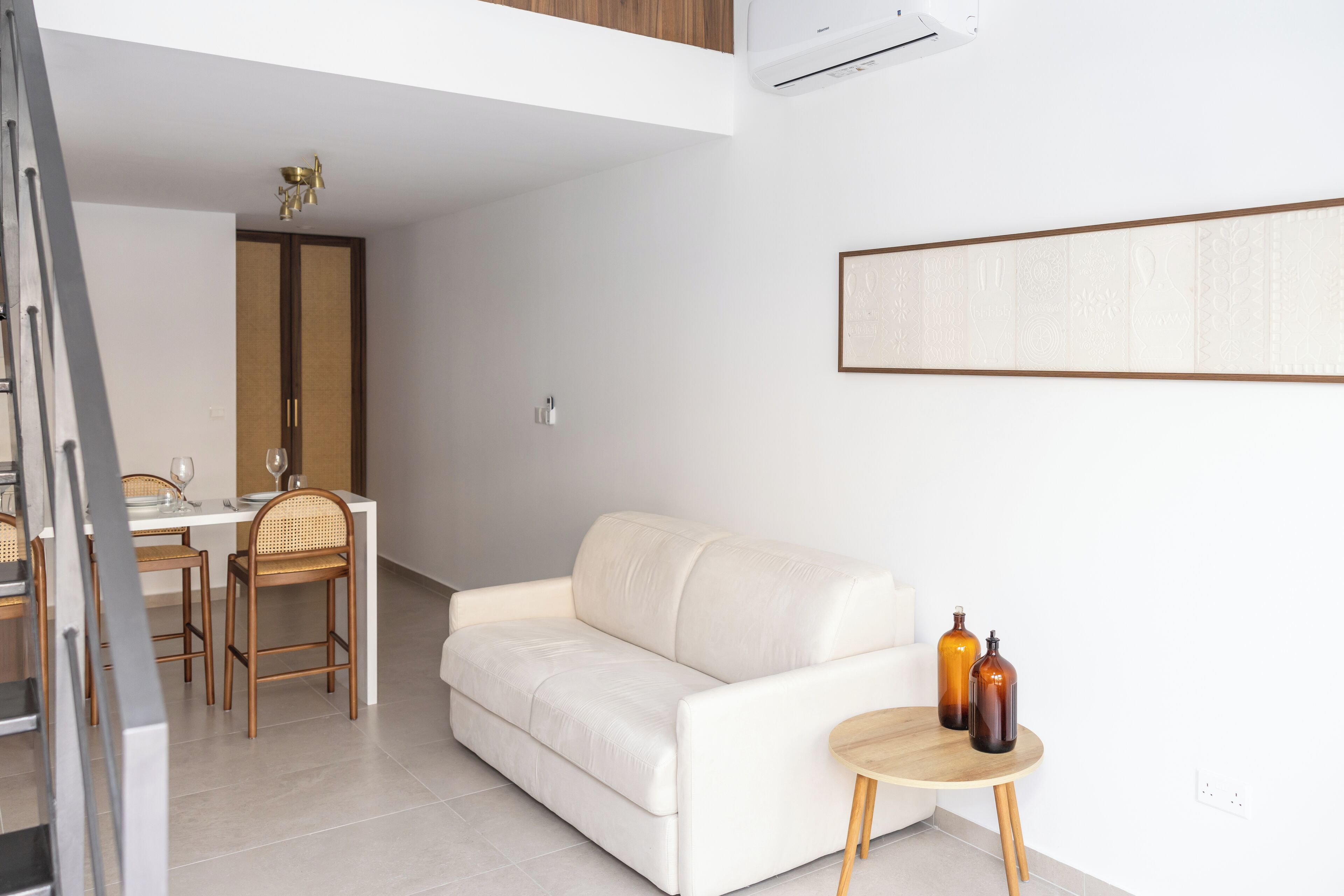 A modern living room with a white sofa, a dining table with chairs, and a small round table with two bottles.