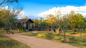 Un chalet rustique, accessible par un chemin de gravier, entouré d’arbres et sous un ciel dégagé.