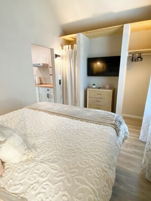 Une chambre avec un grand lit, un téléviseur fixé au mur, une armoire et une petite table sur laquelle est posée une plante.