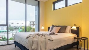 A modern bedroom with a large bed, two bedside lamps, and a view through floor-to-ceiling windows. - Kula Parramatta (MAYS HILL)