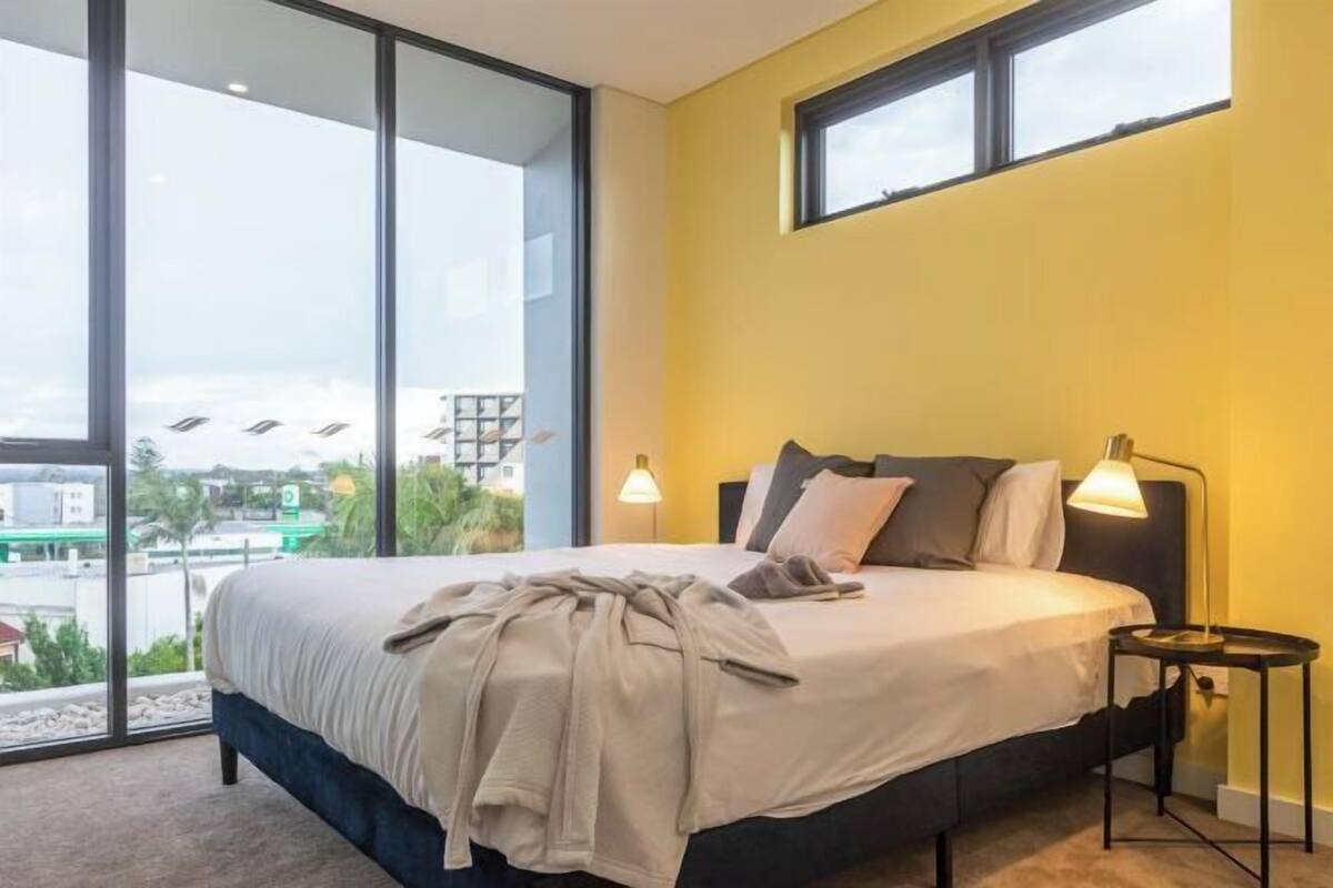 A modern bedroom with a large bed, two bedside lamps, and a view through floor-to-ceiling windows.