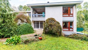 A modern two-story house with a balcony, surrounded by lush greenery and a well-maintained garden.