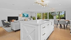 Een moderne keuken met witte kasten, een centraal eiland en een eethoek met een tafel en stoelen.