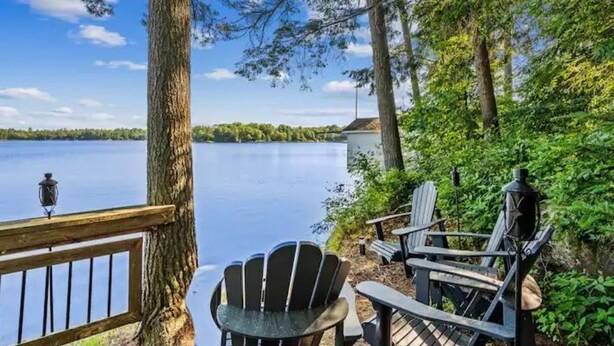 Een terras aan het meer met Adirondack-stoelen en een lantaarn, met uitzicht op een kalm meer.