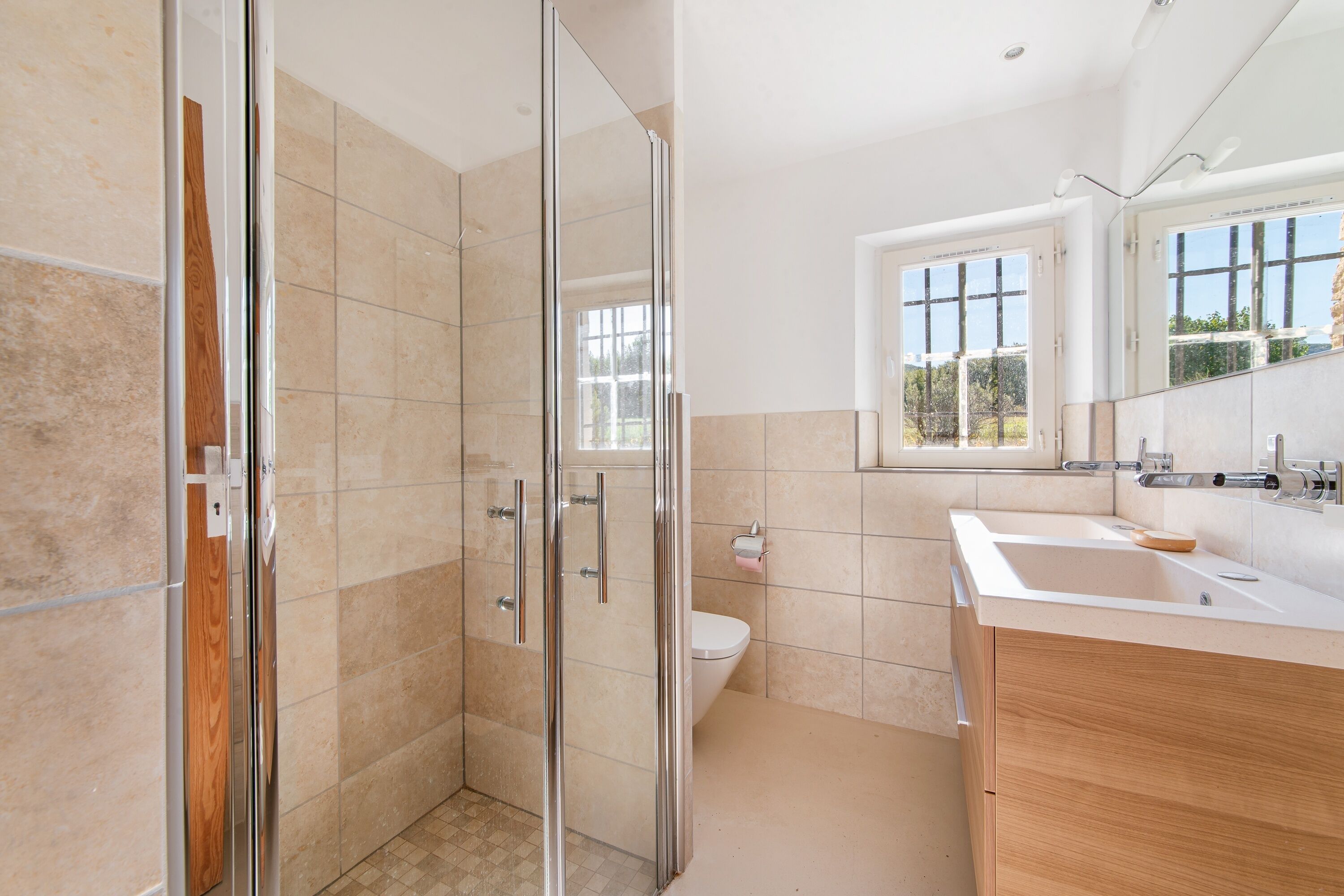 Un baño moderno con cabina de ducha de vidrio, inodoro y lavabo con muebles de madera.