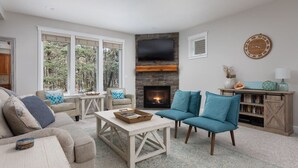 Ein gemütliches Wohnzimmer mit Kamin, bequemen Sitzgelegenheiten und großen Fenstern.