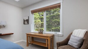 Ein Schlafzimmer mit großem Fenster, Nachttisch aus Holz, einem Sessel und einem Bett.