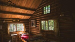 Ein Zimmer in einer Blockhütte mit einem Bett, einem Tisch und zwei Fenstern.