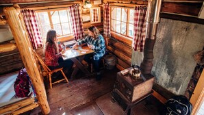 Ein rustikales Blockhaus-Interieur mit Holzwänden, einem Holztisch und einem alten Herd.
