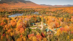 Eine Lodge, umgeben von einem Wald mit Herbstlaub, einem See und Bergen im Hintergrund.