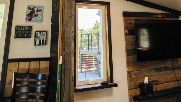 A room with a sloped ceiling, wooden beams, a TV mounted on the wall, and a window with a view of the outside. - Colorado Cottage located at 7200 feet, near to Colorado Springs. (Elbert)