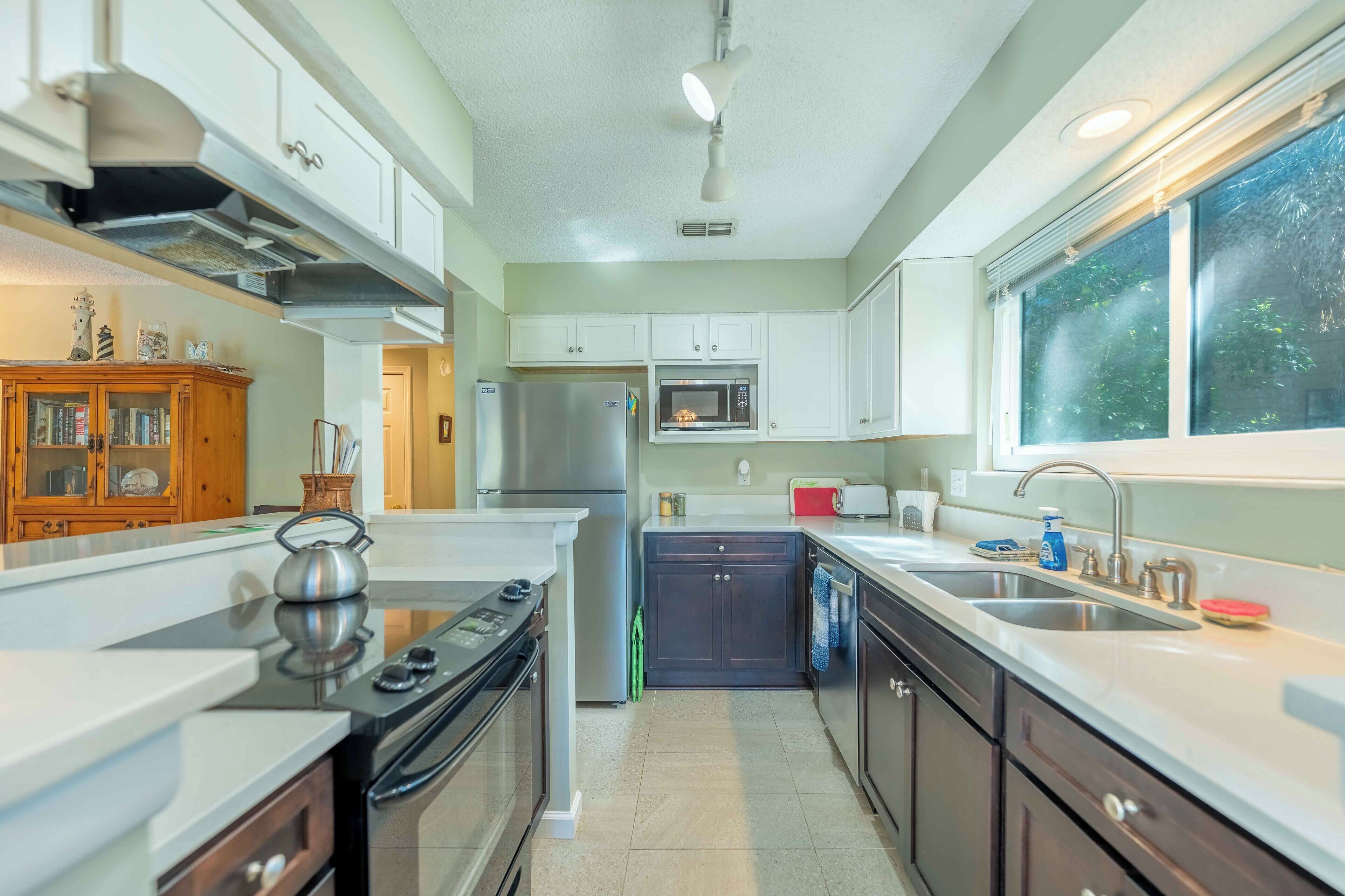 A modern kitchen with stainless steel appliances, white cabinetry, and a large window providing natural light.