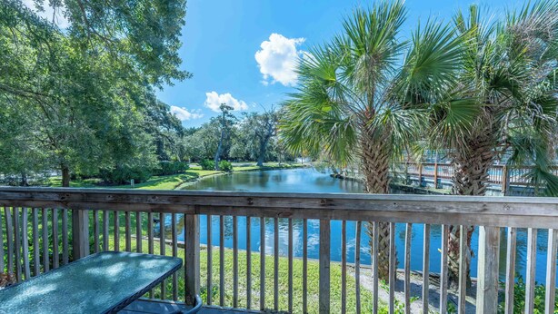 A wooden deck with a table and chairs overlooking a pond surrounded by trees and palm trees. - 2681 Forest Ridge B1 | 2BR Condo with Water Views (Fernandina Beach)