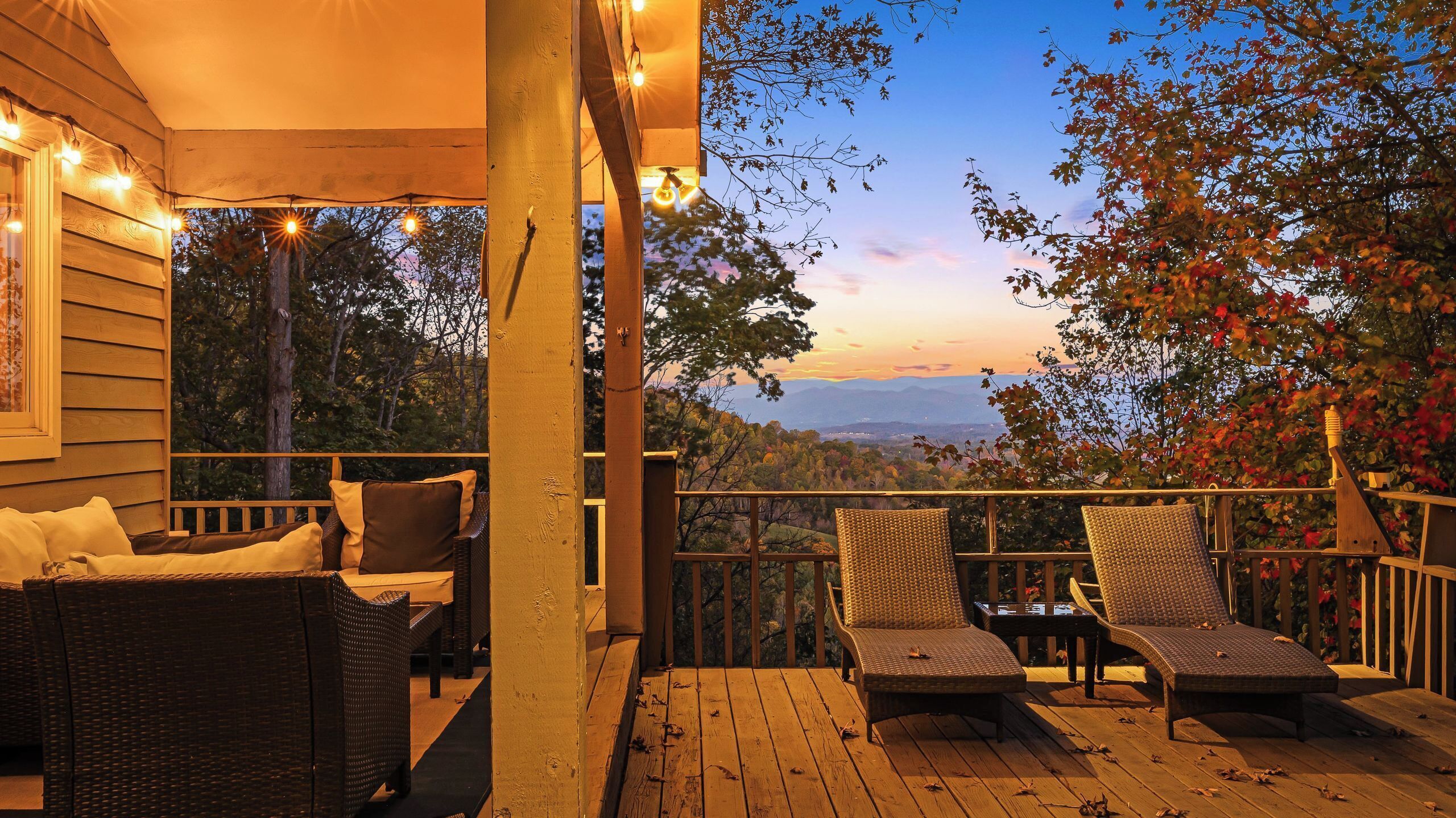A wooden deck with wicker furniture and string lights, overlooking a scenic landscape.