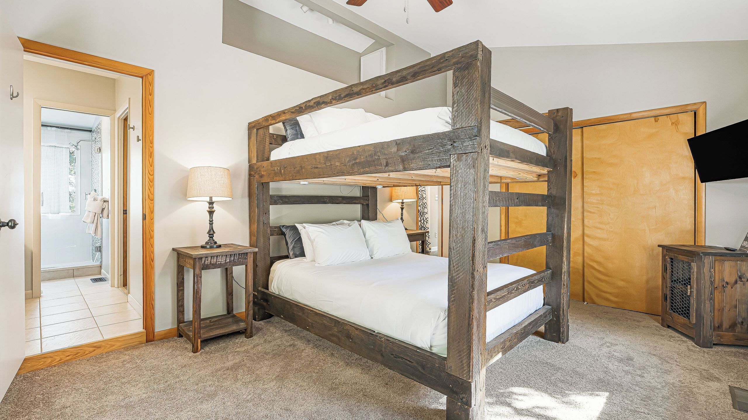 A bunk bed with a wooden frame, a bedside table with a lamp, a shower area, and a television.