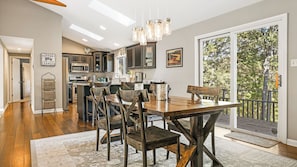A modern kitchen with dark cabinetry, a central island, and a dining area with a wooden table and chairs. - Cabin in the Sky by Avantstay Deck w/ Views (Leicester)