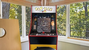 A Pac-Man arcade machine with a maze game, located near a window with a view of trees. - Cabin in the Sky by Avantstay Deck w/ Views (Leicester)