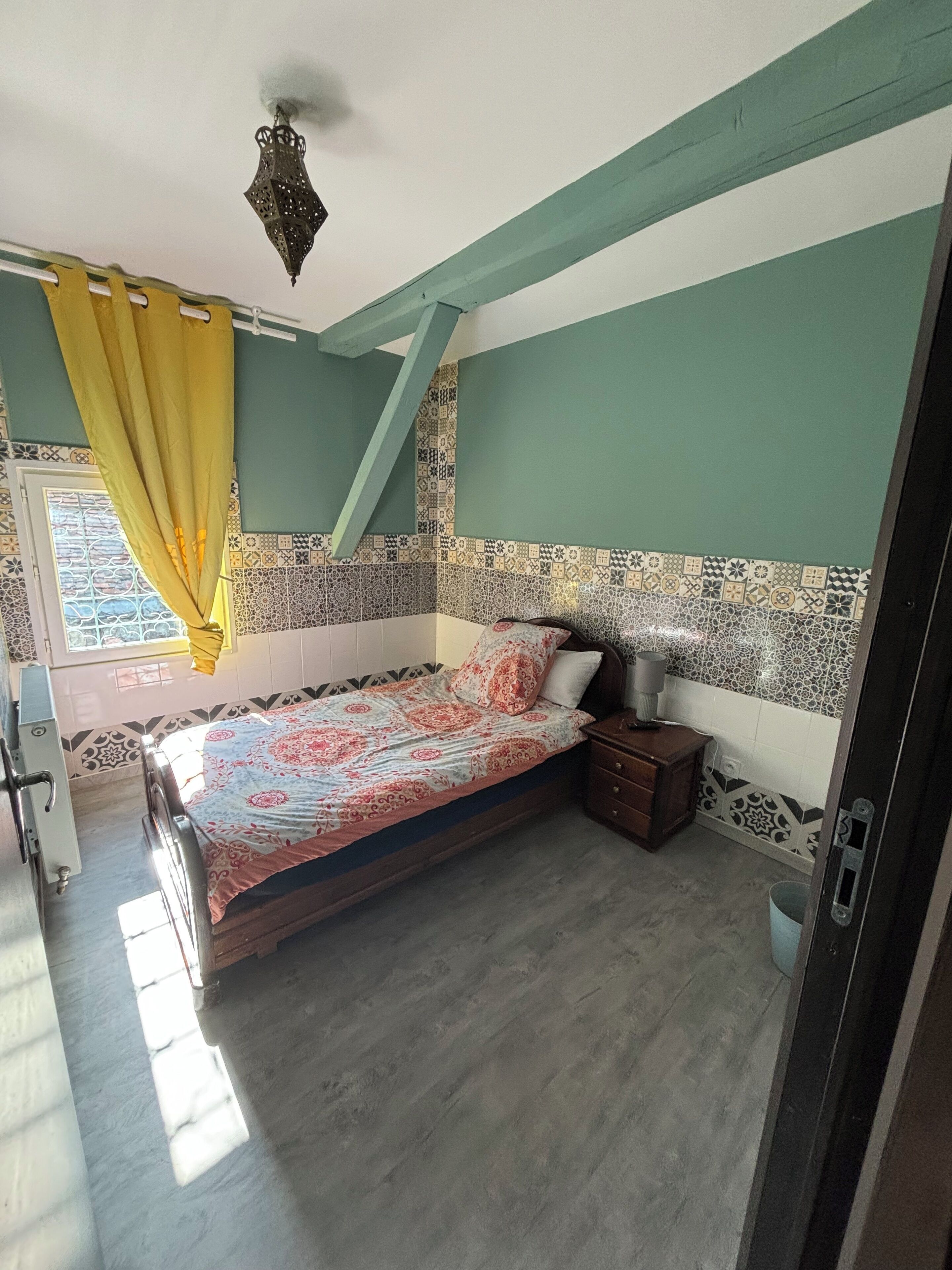 A bedroom with a bed, a nightstand, a ceiling fan, and a window with curtains.