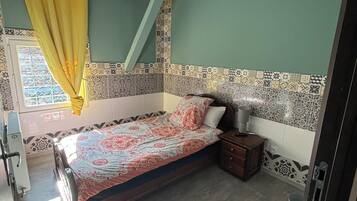 A bedroom with a bed, a nightstand, a ceiling fan, and a window with curtains.