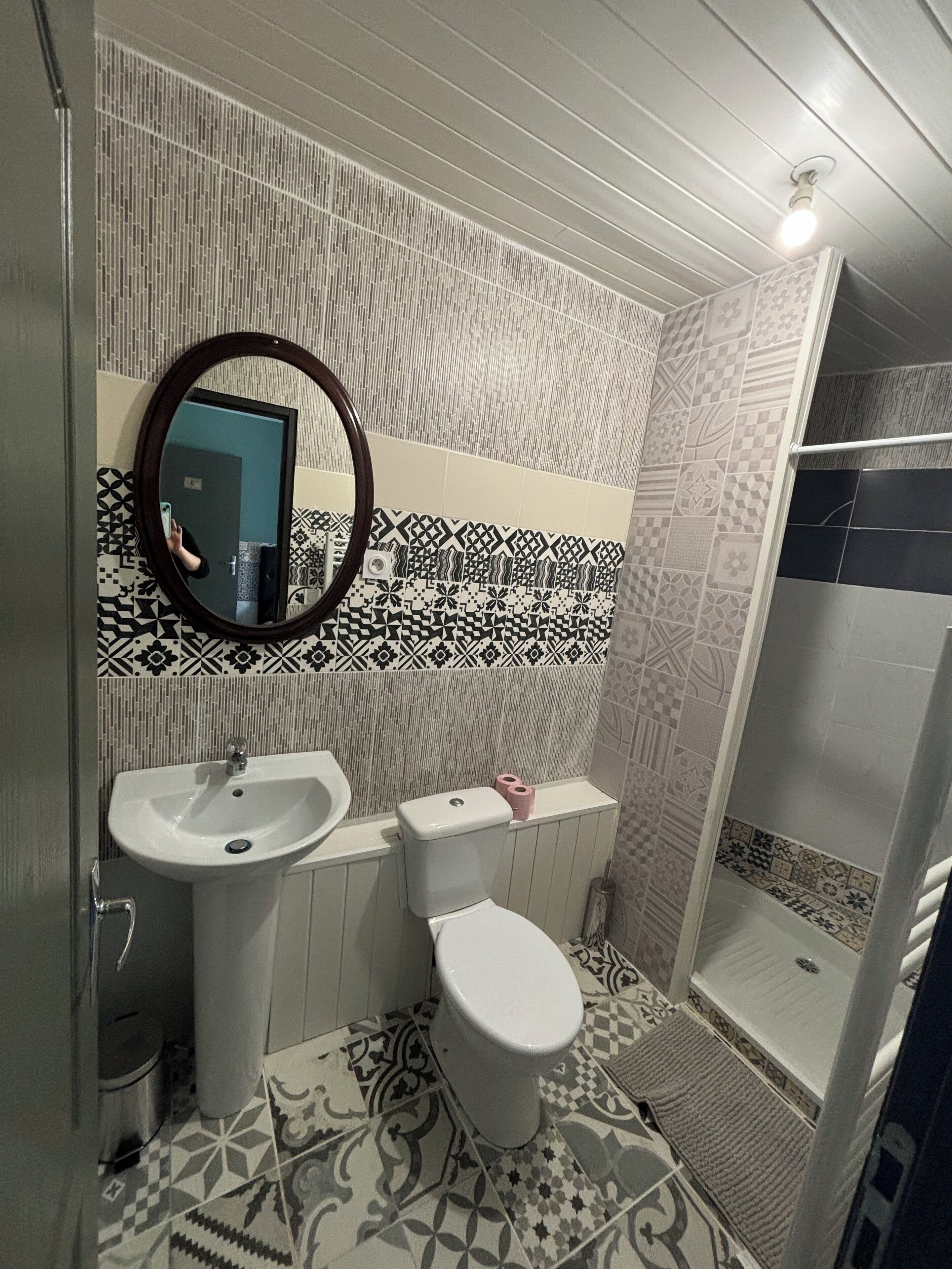 Baño con lavamanos, inodoro y ducha. Las paredes tienen azulejos con diseño, y hay un espejo sobre el lavamanos.