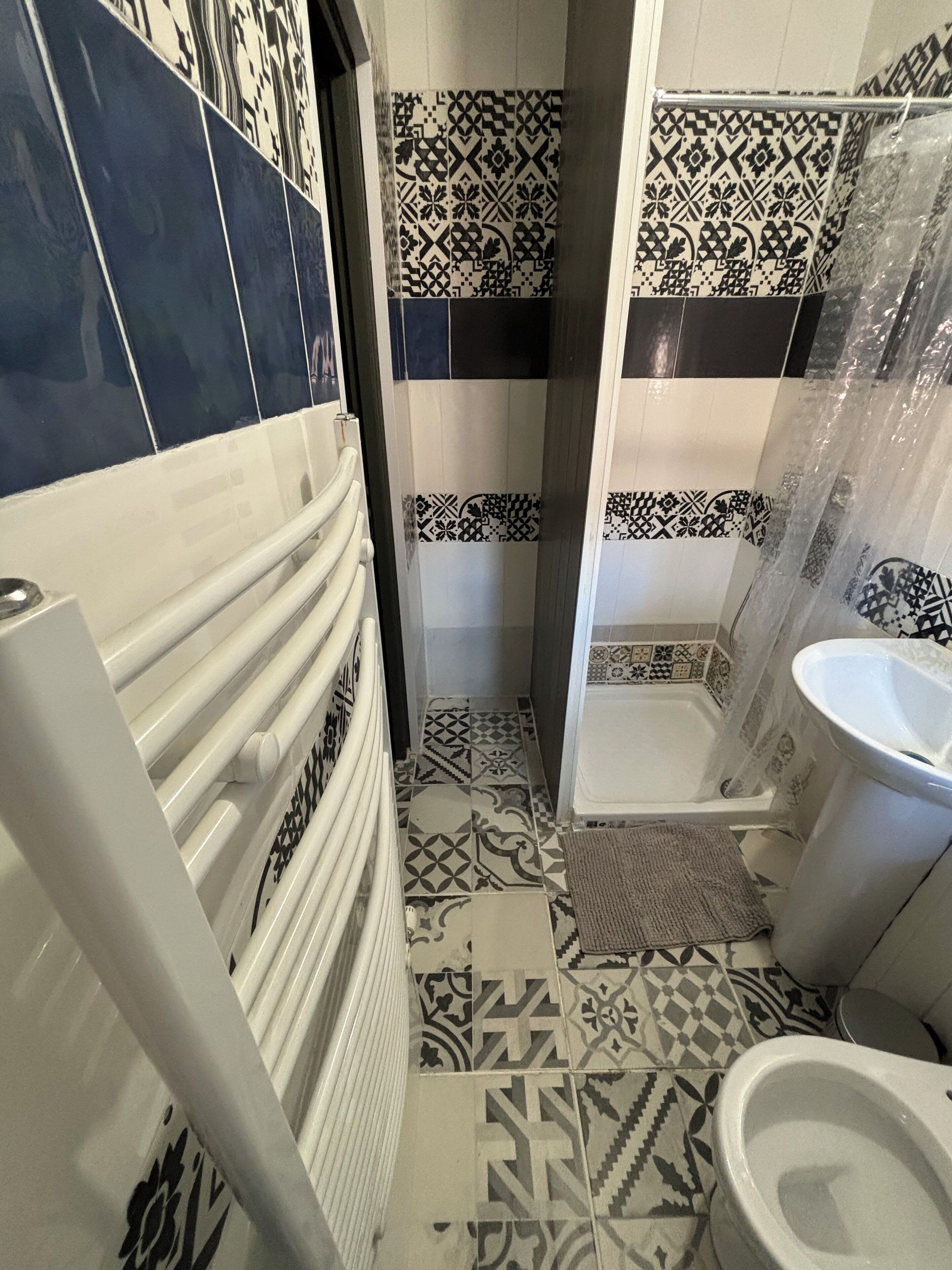 A bathroom with patterned tiles, a white radiator, a shower area, and a toilet.