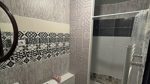 Un baño con inodoro, bid é y ducha. Las paredes están cubiertas de azulejos con diseños geométricos.