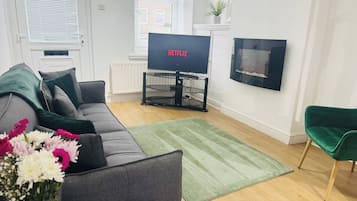 Un soggiorno con un divano grigio, un tappeto verde, una TV a schermo piatto e una poltrona verde.