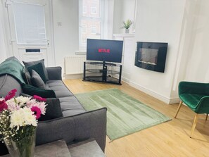 Una sala de estar con un sofá gris, una alfombra verde, un televisor de pantalla plana y un sillón verde.