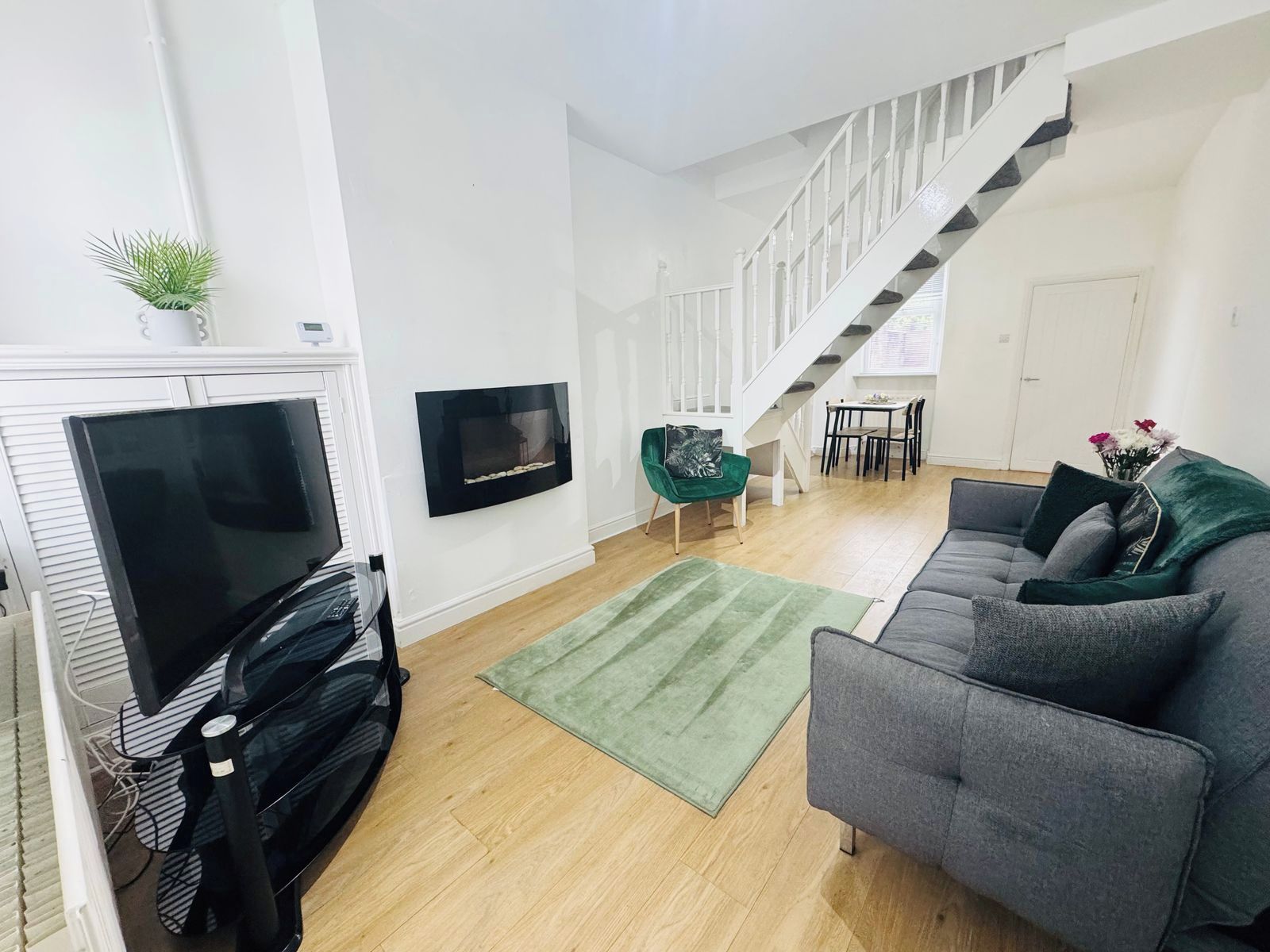 Ein modernes Wohnzimmer mit Flachbildfernseher, Kamin, Treppe und einem grauen Sofa.