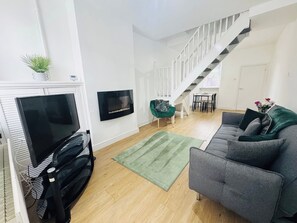 En moderne stue med et fladskærms-tv, pejs, trappe og en grå sofa.